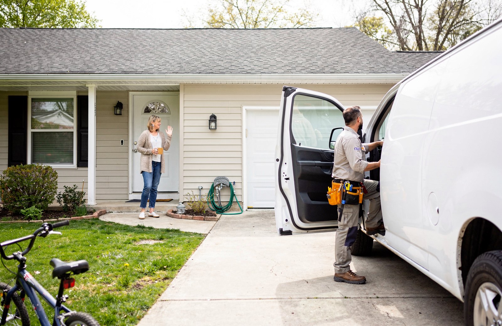 A service van arriving in a driveway while the homeowner waves from the step